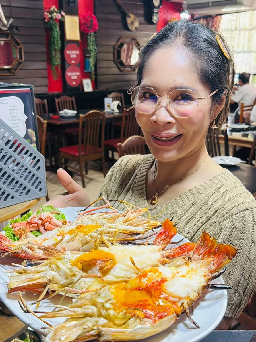 The owner holding out a large platter of split grilled river prawns in the dining room, the MICHELIN plaques on the wall behind her.